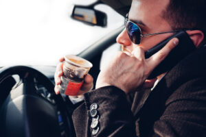 man drinking coffee and using mobile phone while driving car