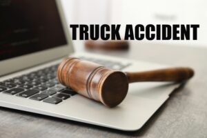 Truck accident law. Laptop and judge's gavel on table indoors, closeup